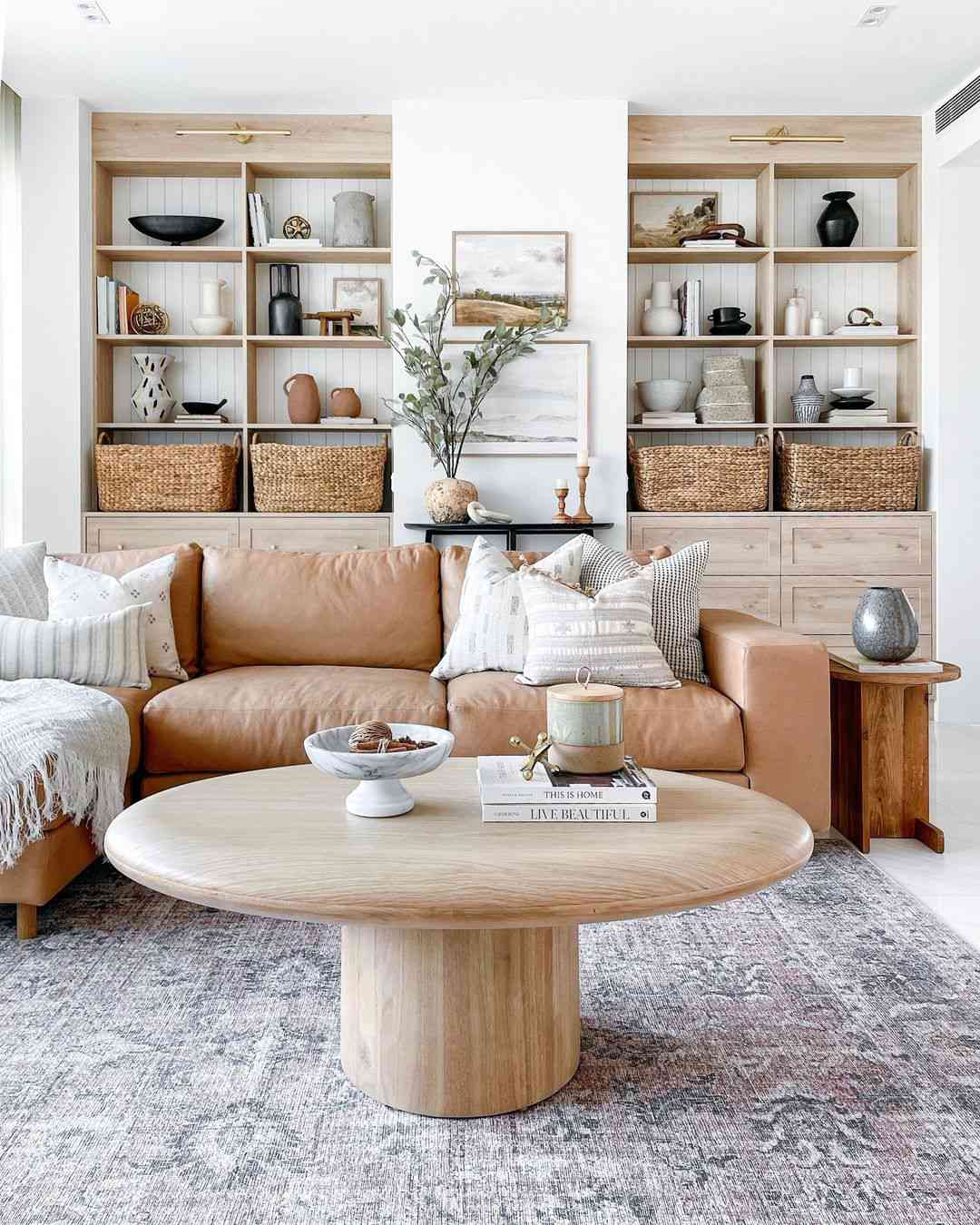 A neutral living room with a warm brown sofa, wooden cabinets and furniture, and layered soft furnishings in white and gray striped and block patterns