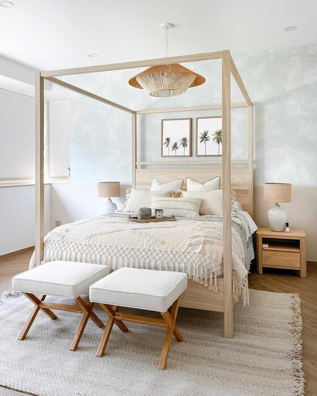 A soft, tropical bedroom with a light green palm wallpaper and cozy, layered four-post bed