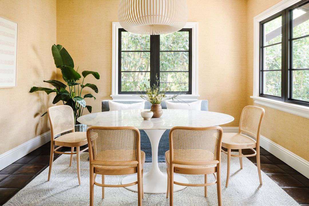 Small yellow dining room with white pedestal table and cane bentwood chairs