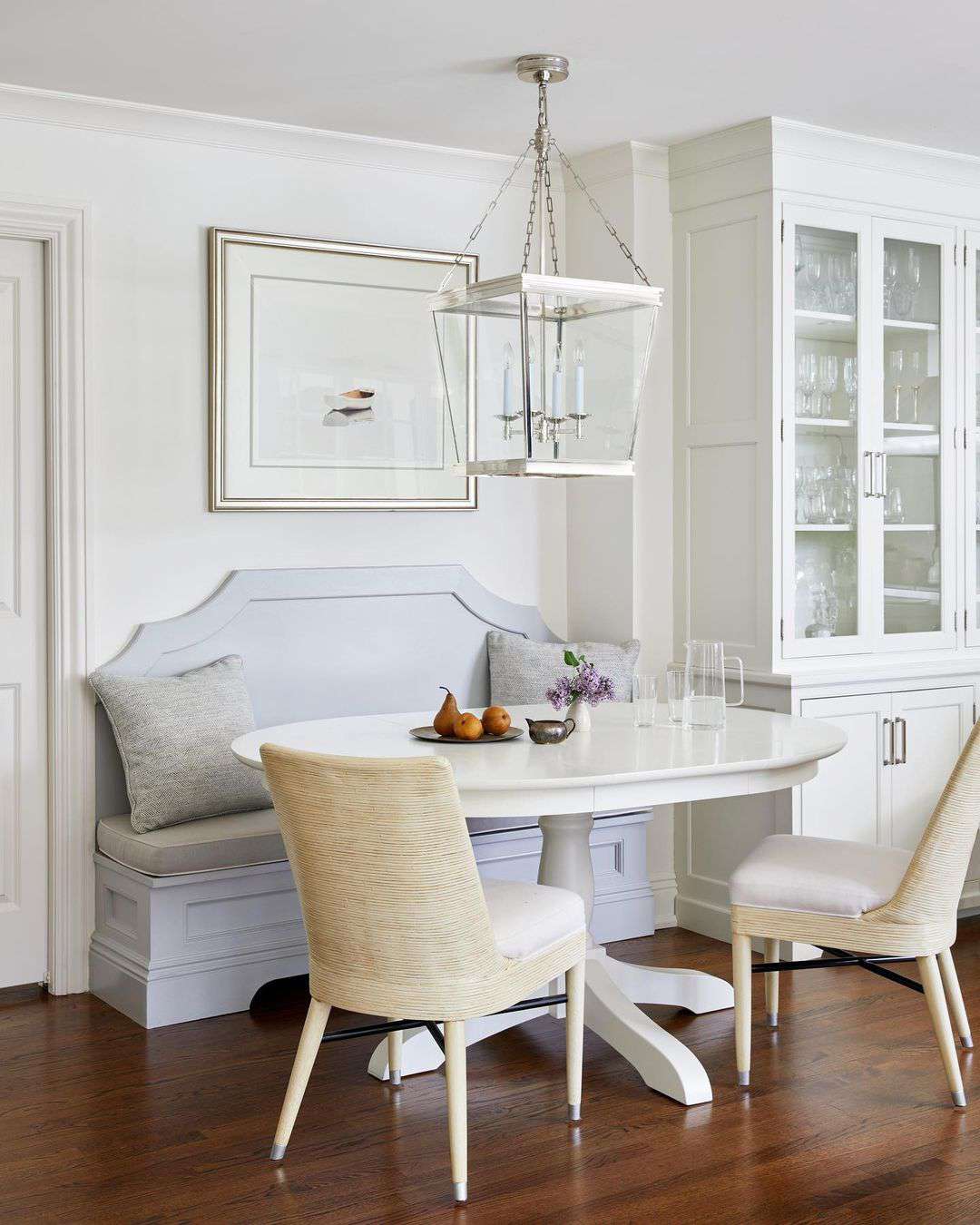 Elegant classic white dining room with built in wood banquet, white wood pedestal dining table, and yellow textured slipper dining chairs