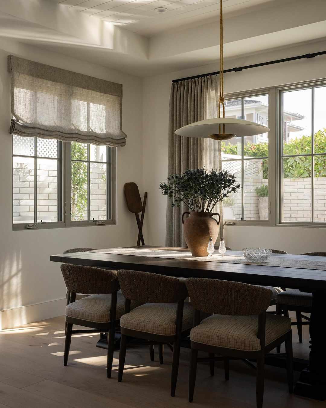 Modern rustic dining room with industrial modern pendant light, farm table, rattan wrapped dining chairs, and stone urn filled with thistle