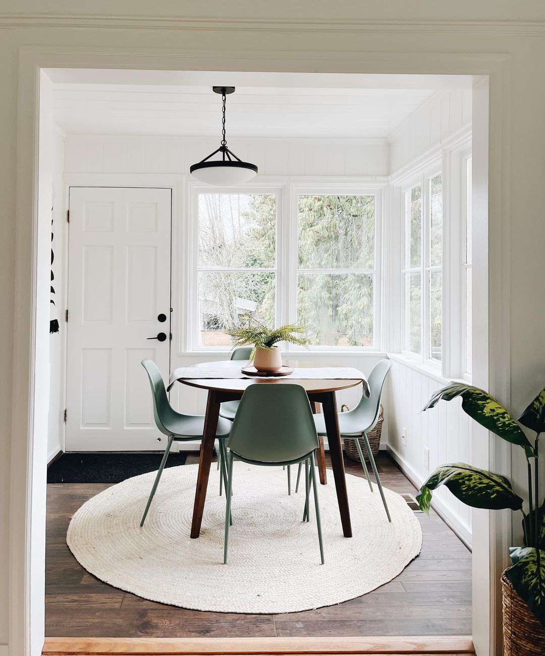 Small dining room with green Eames style chairs, round wood Mid-Century Modern table, and round rug